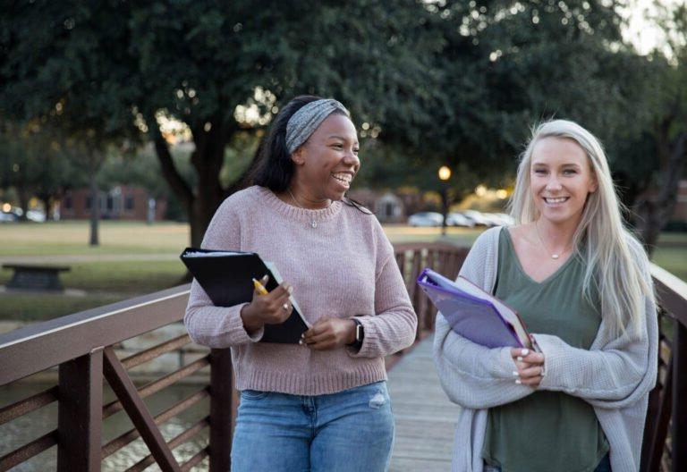 Photo of two smiling HSU students crossing a foot bridge on campus.